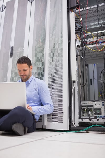 Man working with his laptop on the floor beside servers in data center